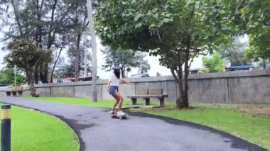 Güzel genç bir kadın ustalıkla kaykayla parktan geçiyor.