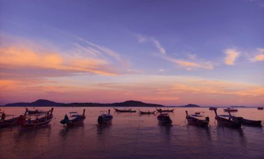 Nefis, sakin bir gün batımı manzarası. Dalgalı gökyüzüne karşı zarifçe siluetlenmiş balıkçı tekneleri.