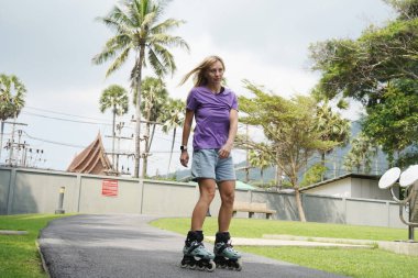 Bir kadın, güzel bir park ortamında uzanan manzaralı bir yolda paten kaymaktan zevk alıyor..
