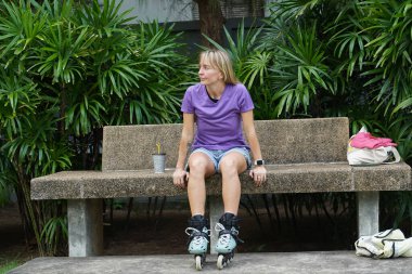 Bir kadın bankta oturuyor, patenlerini takıyor..