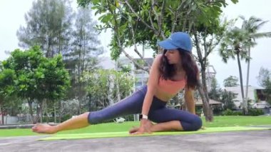 Genç bir kadın güzel bir şehir parkında yoga minderi yapıyor.