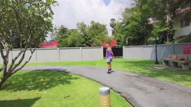 Bir kadın, güzel bir park ortamında uzanan manzaralı bir yolda paten kaymaktan zevk alıyor..