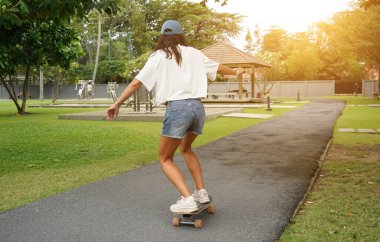 Güzel genç bir kadın ustalıkla kaykayla parktan geçiyor.