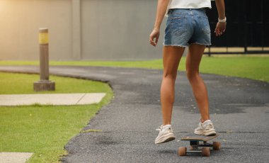 Güzel genç bir kadın ustalıkla kaykayla parktan geçiyor.