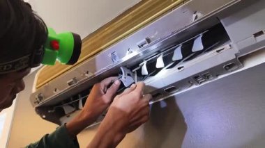 Bir teknisyen duvara monte edilmiş klimayı tamir eder ve havalandırma sistemini tamir eder.. 