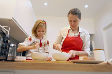 Anne ve kızı geleneksel Ukrayna kostümleriyle mutfakta Paskalya için kek yapıyorlar..