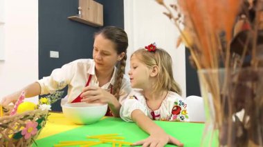 Anne ve kızı geleneksel Ukrayna kostümleriyle Paskalya için yumurta boyuyor..