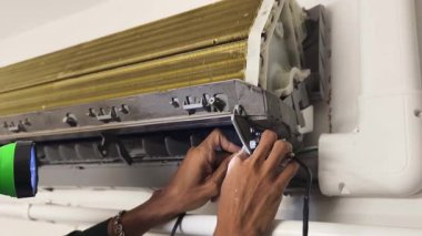 Bir teknisyen duvara monte edilmiş klimayı tamir eder ve havalandırma sistemini tamir eder.. 