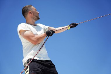 Yelkenlinin güvertesinde erkek kaptan yelkenleri açıyor halatı çekiyor.