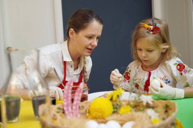 Anne ve kızı geleneksel Ukrayna kostümleriyle Paskalya için yumurta boyuyor..
