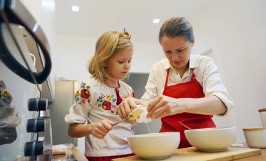 Anne ve kızı geleneksel Ukrayna kostümleriyle mutfakta Paskalya için kek yapıyorlar..