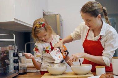 Anne ve kızı geleneksel Ukrayna kostümleriyle mutfakta Paskalya için kek yapıyorlar..