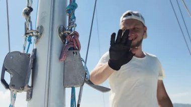 Yelkenlinin güvertesinde erkek kaptan yelkenleri açıyor halatı çekiyor.