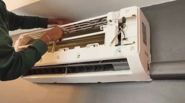 Bir teknisyen duvara monte edilmiş klimayı tamir eder ve havalandırma sistemini tamir eder.. 