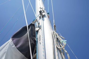 Yelkenlinin uzun ve sağlam direği parlak mavi gökyüzüne karşı canlı bir şekilde duruyor.