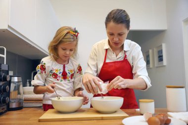 Anne ve kızı geleneksel Ukrayna kostümleriyle mutfakta Paskalya için kek yapıyorlar..