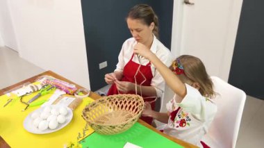 Anne ve kızı geleneksel Ukrayna kostümleriyle Paskalya için sepet dokuyorlar..