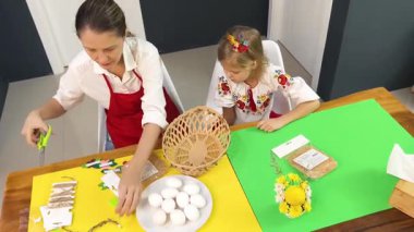 Anne ve kızı geleneksel Ukrayna kostümleriyle Paskalya için sepet dokuyorlar..