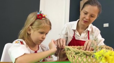 Anne ve kızı geleneksel Ukrayna kostümleriyle Paskalya için sepet dokuyorlar..