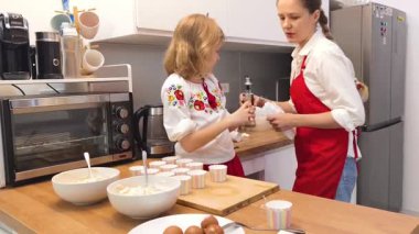 Anne ve kızı geleneksel Ukrayna kostümleriyle mutfakta Paskalya için kek yapıyorlar..