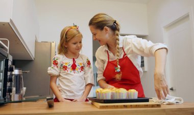 Anne ve kızı geleneksel Ukrayna kostümleriyle mutfakta Paskalya için kek yapıyorlar..