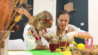 Anne ve kızı geleneksel Ukrayna kostümleriyle Paskalya için yumurta boyuyor..