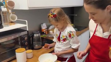 Anne ve kızı geleneksel Ukrayna kostümleriyle mutfakta Paskalya için kek yapıyorlar..