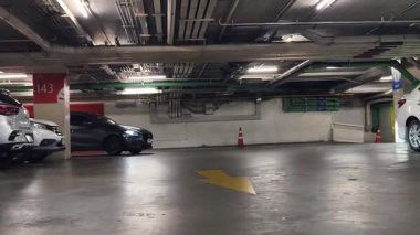 Bir araba, çeşitli koni ve tabelalarla işaretlenmiş park alanından dikkatle geçiyor..