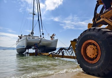 Sarı traktör güzel bir sahil bölgesinde sudan bir tekne çıkarıyor..