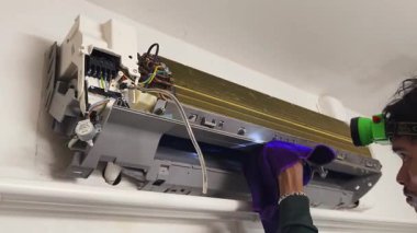 Bir teknisyen duvara monte edilmiş klimayı tamir eder ve havalandırma sistemini tamir eder.. 