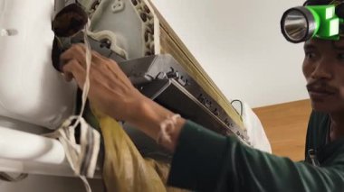 Bir teknisyen duvara monte edilmiş klimayı duruluyor ve havalandırma sistemini tamir ediyor..