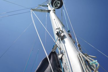 Yelkenlinin uzun ve sağlam direği parlak mavi gökyüzüne karşı canlı bir şekilde duruyor.