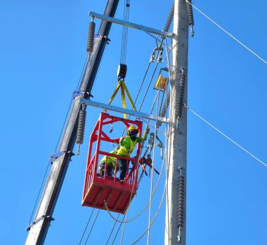 İş kıyafetleri ve şapkalı adamlar elektrik direğine yüksek voltajlı kablolar yerleştiriyor..