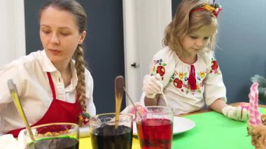 Anne ve kızı geleneksel Ukrayna kostümleriyle Paskalya için yumurta boyuyor..