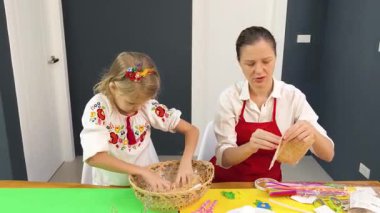 Anne ve kızı geleneksel Ukrayna kostümleriyle Paskalya için sepet dokuyorlar..