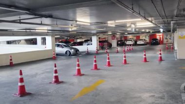 Bir araba, çeşitli koni ve tabelalarla işaretlenmiş park alanından dikkatle geçiyor..