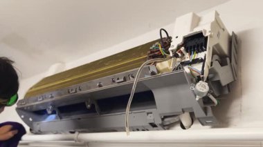 Bir teknisyen duvara monte edilmiş klimayı tamir eder ve havalandırma sistemini tamir eder.. 