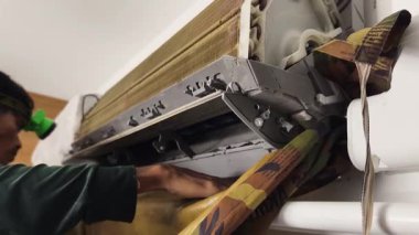 Bir teknisyen duvara monte edilmiş klimayı duruluyor ve havalandırma sistemini tamir ediyor..