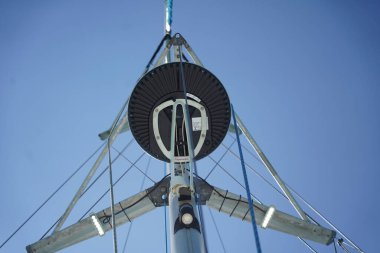 Yelkenlinin uzun ve sağlam direği parlak mavi gökyüzüne karşı canlı bir şekilde duruyor.