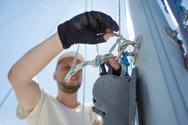 Yelkenlinin güvertesinde erkek kaptan yelkenleri açıyor halatı çekiyor.