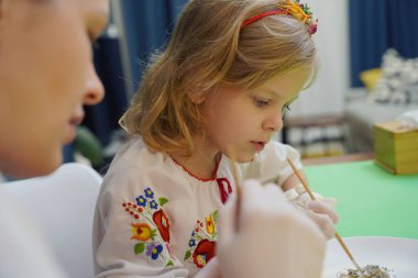 Anne ve kızı geleneksel Ukrayna kostümleriyle Paskalya için yumurta boyuyor..