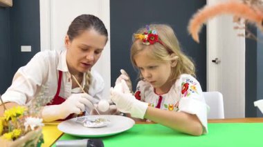 Anne ve kızı geleneksel Ukrayna kostümleriyle Paskalya için yumurta boyuyor..