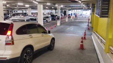 Bir araba, çeşitli koni ve tabelalarla işaretlenmiş park alanından dikkatle geçiyor..