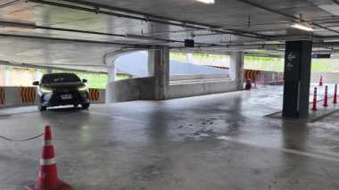 Bir araba, çeşitli koni ve tabelalarla işaretlenmiş park alanından dikkatle geçiyor..