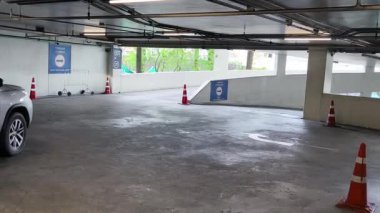 Bir araba, çeşitli koni ve tabelalarla işaretlenmiş park alanından dikkatle geçiyor..