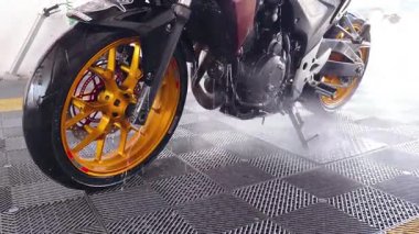 Bir motosiklet titiz bir temizlikten geçer, göz kamaştırıcı altın tekerleklerini vurgular..