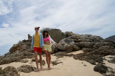 Genç bir çift kumsalda boş boş yürüyor, el ele tutuşuyor ve sıcak güneşin tadını çıkarıyor..