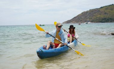 Genç çift, açık mavi bir kanoyla birlikte sarı raketlerle mutlu bir şekilde yol alıyorlar..