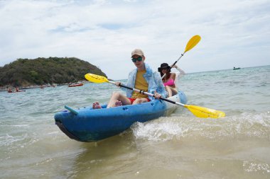 Genç çift, açık mavi bir kanoyla birlikte sarı raketlerle mutlu bir şekilde yol alıyorlar..