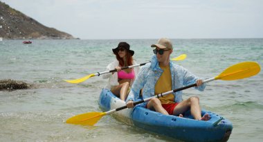 Genç çift, açık mavi bir kanoyla birlikte sarı raketlerle mutlu bir şekilde yol alıyorlar..